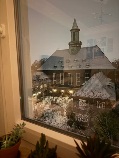 Blick aus einem Fenster auf eine Dorfkirche mit Turm in der winterlichen Abenddämmerung