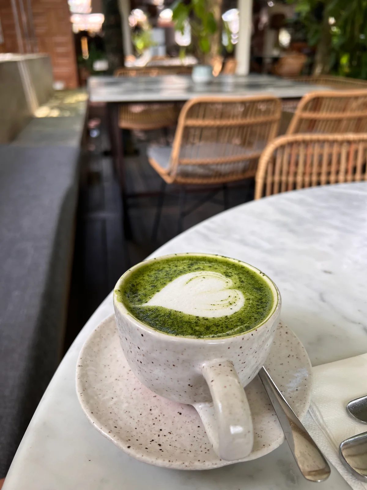 Ein Matcha Latte mit Herz-Latte-Art in einer gesprenkelten Keramiktasse auf einem Marmortisch