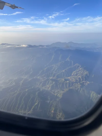 Blick aus dem Flugzeugfenster auf eine Bergkette, die aus dem Dunst ragt