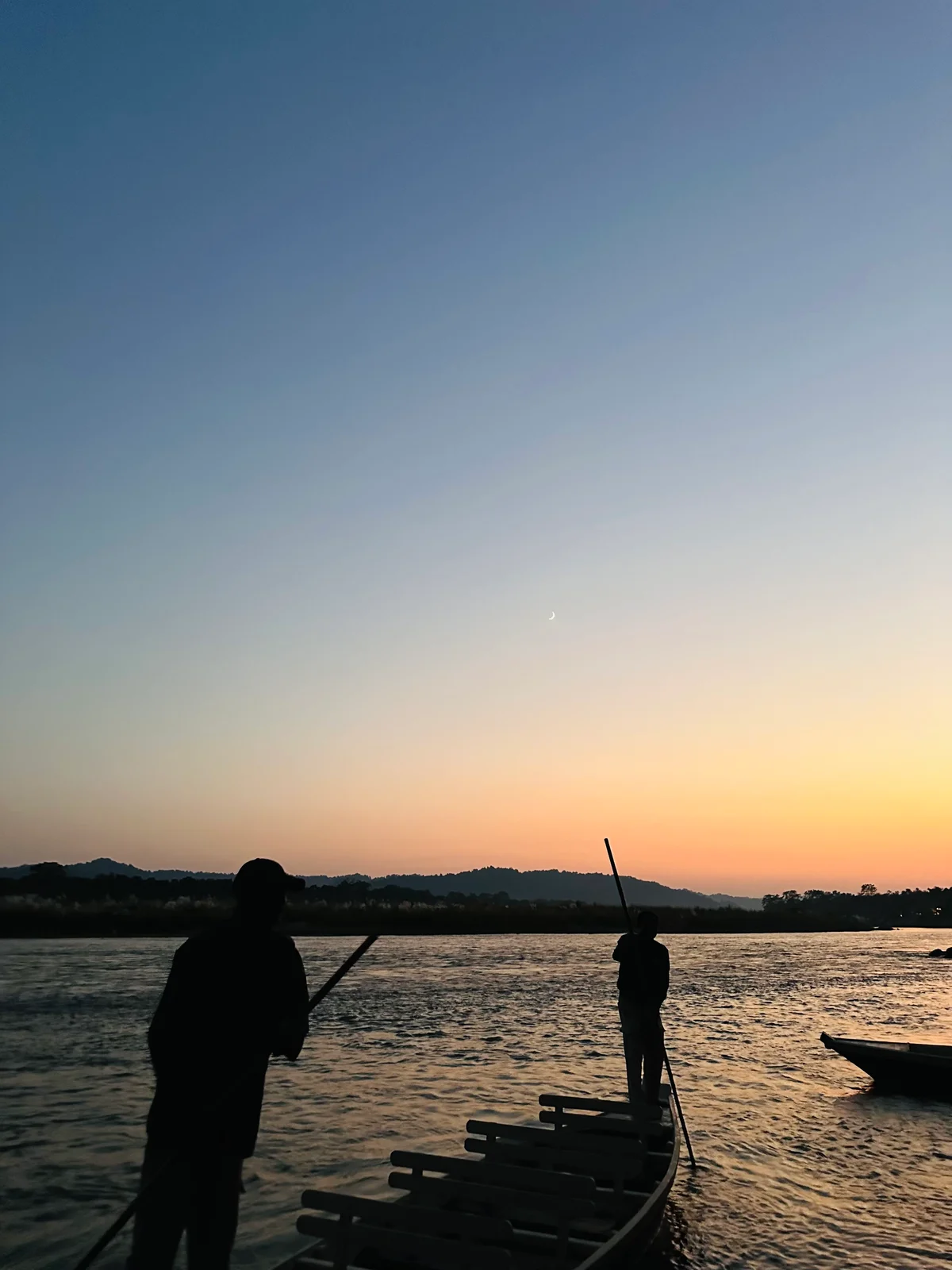 Silhouetten von Fährleuten auf einem Floß bei Sonnenuntergang über einem ruhigen Fluss