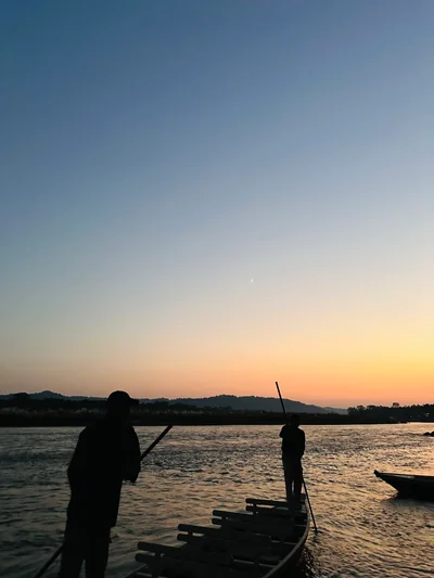 Silhouetten von Fährleuten auf einem Floß bei Sonnenuntergang über einem ruhigen Fluss