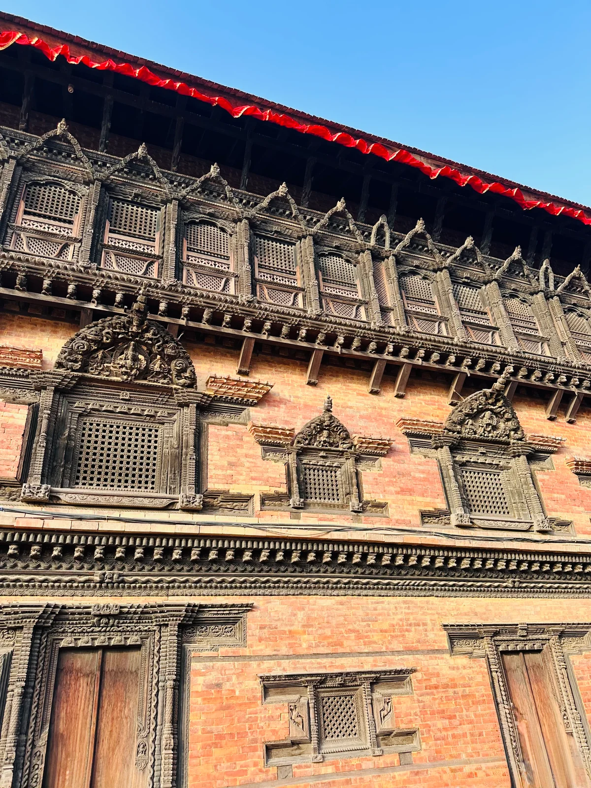 Kunstvoll geschnitzte Holzfenster und Gitter an einer traditionellen nepalesischen Ziegelfassade