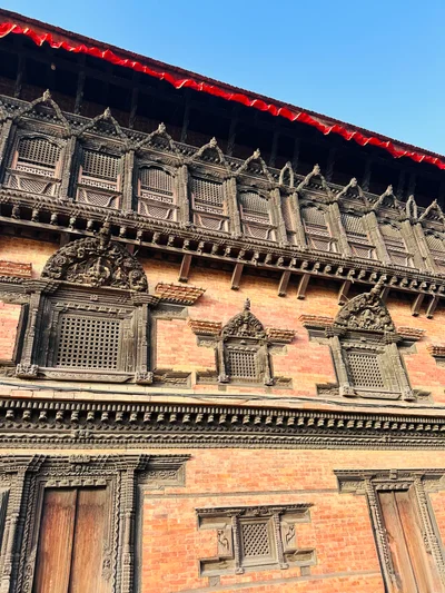 Kunstvoll geschnitzte Holzfenster und Gitter an einer traditionellen nepalesischen Ziegelfassade