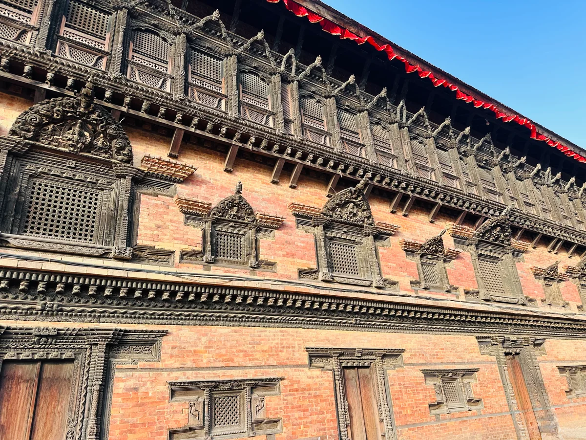 Detailreiche Holzschnitzerei an der Backsteinfassade eines historischen nepalesischen Palastes