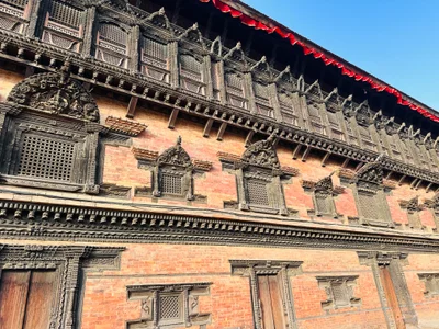 Detailreiche Holzschnitzerei an der Backsteinfassade eines historischen nepalesischen Palastes