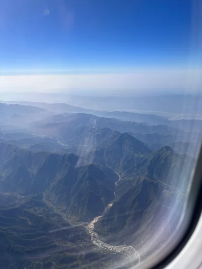 Blick aus dem Flugzeugfenster auf eine zerklüftete Berglandschaft unter klarem Himmel