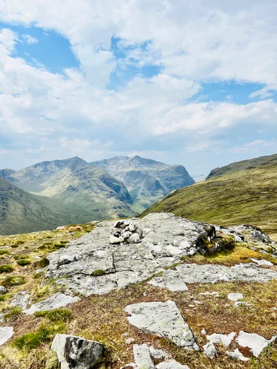 Felsplateau auf einem schottischen Berggipfel mit Blick auf grüne Berge unter weißen Wolken