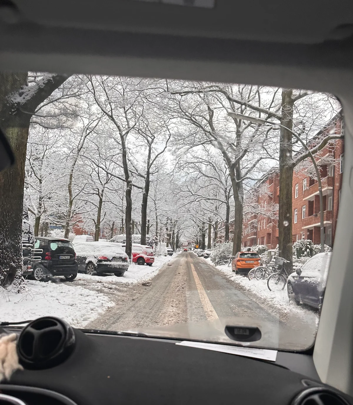 Blick aus einem Auto auf eine verschneite Hamburger Allee mit alten Bäumen und Backsteinhäusern