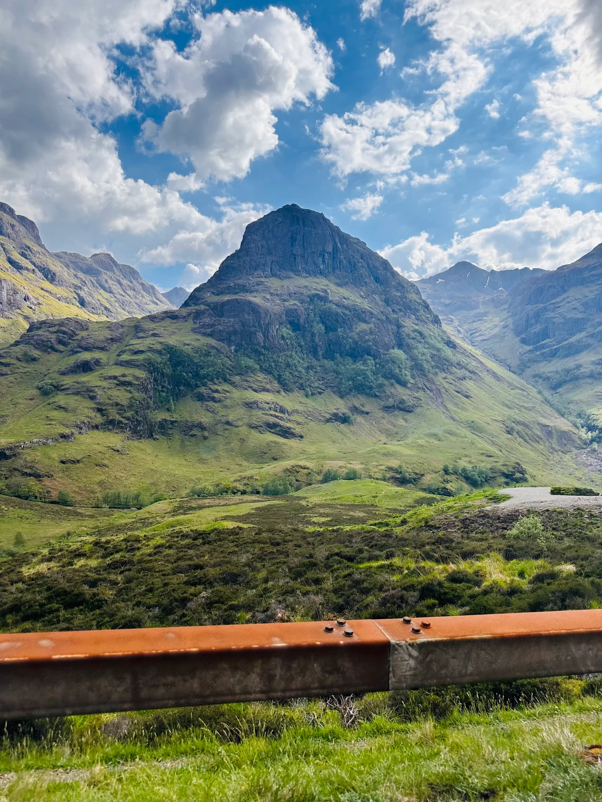 Ein markanter Berggipfel in Glen Coe ragt hinter einer rostigen Leitplanke in den Himmel