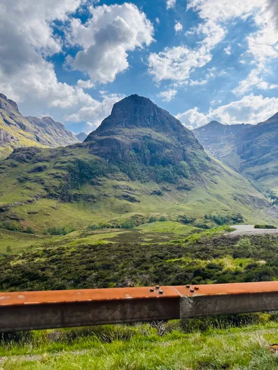 Ein markanter Berggipfel in Glen Coe ragt hinter einer rostigen Leitplanke in den Himmel