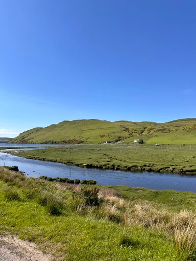 Eine schmale Straße führt durch saftig grüne schottische Highlands unter blauem Himmel