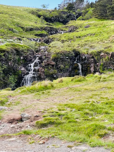 Ein kleiner Wasserfall stürzt über Felsen in einem saftig grünen Hügeltal