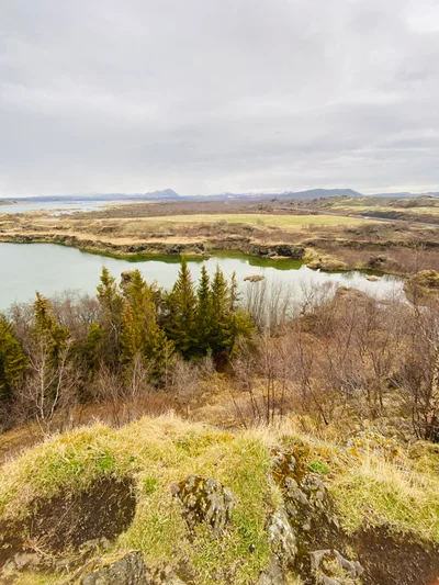 Blick über einen grünblauen See und karge Vegetation auf eine isländische Berglandschaft